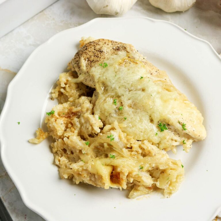 Baked chicken breast topped with melted cheese served over creamy rice on a white plate, garnished with chopped herbs.
