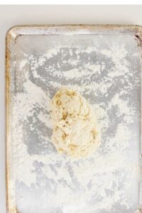 A mound of biscuit dough sits on a floured metal baking sheet.