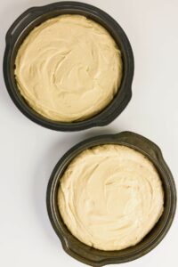Two round cake pans filled with unbaked cake batter are placed side by side on a white surface.