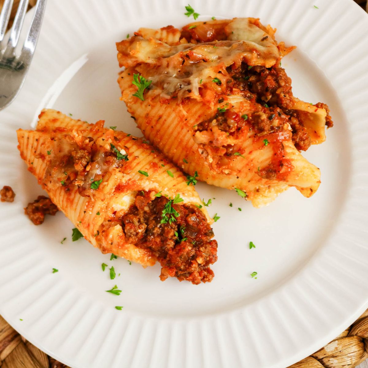 Two stuffed pasta shells filled with meat sauce and topped with melted cheese, garnished with chopped parsley, served on a white plate.