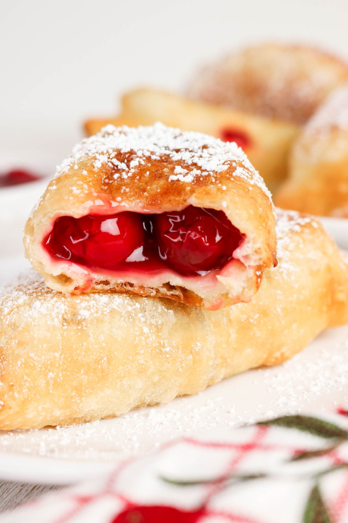 A close-up of a cherry-filled pastry topped with powdered sugar, with one pastry cut open to reveal the bright red cherry filling.