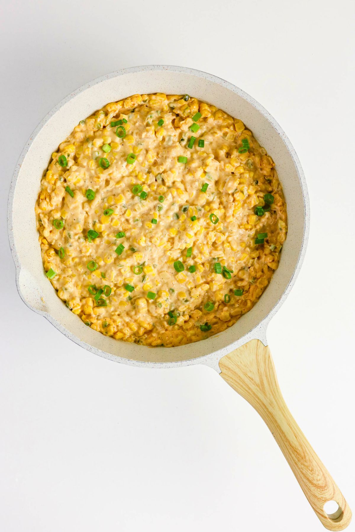 A white skillet filled with creamy corn dip topped with chopped green onions, viewed from above on a white background.