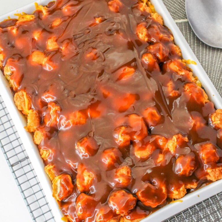 A rectangular baking dish filled with bread pudding topped with a glossy layer of chocolate sauce, placed on a cooling rack next to a metal serving spoon.