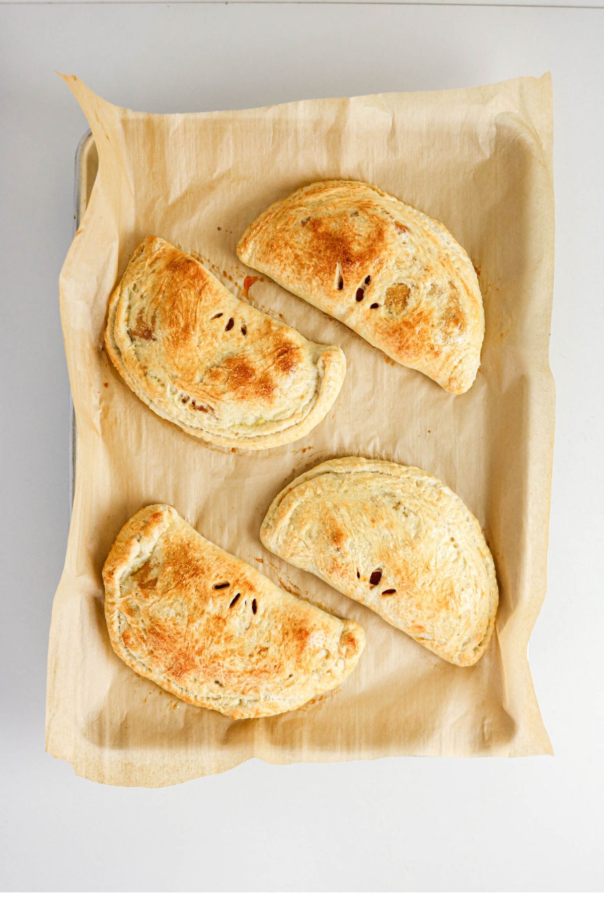 Four baked pastries with golden-brown tops are arranged on a parchment-lined baking sheet, viewed from above.