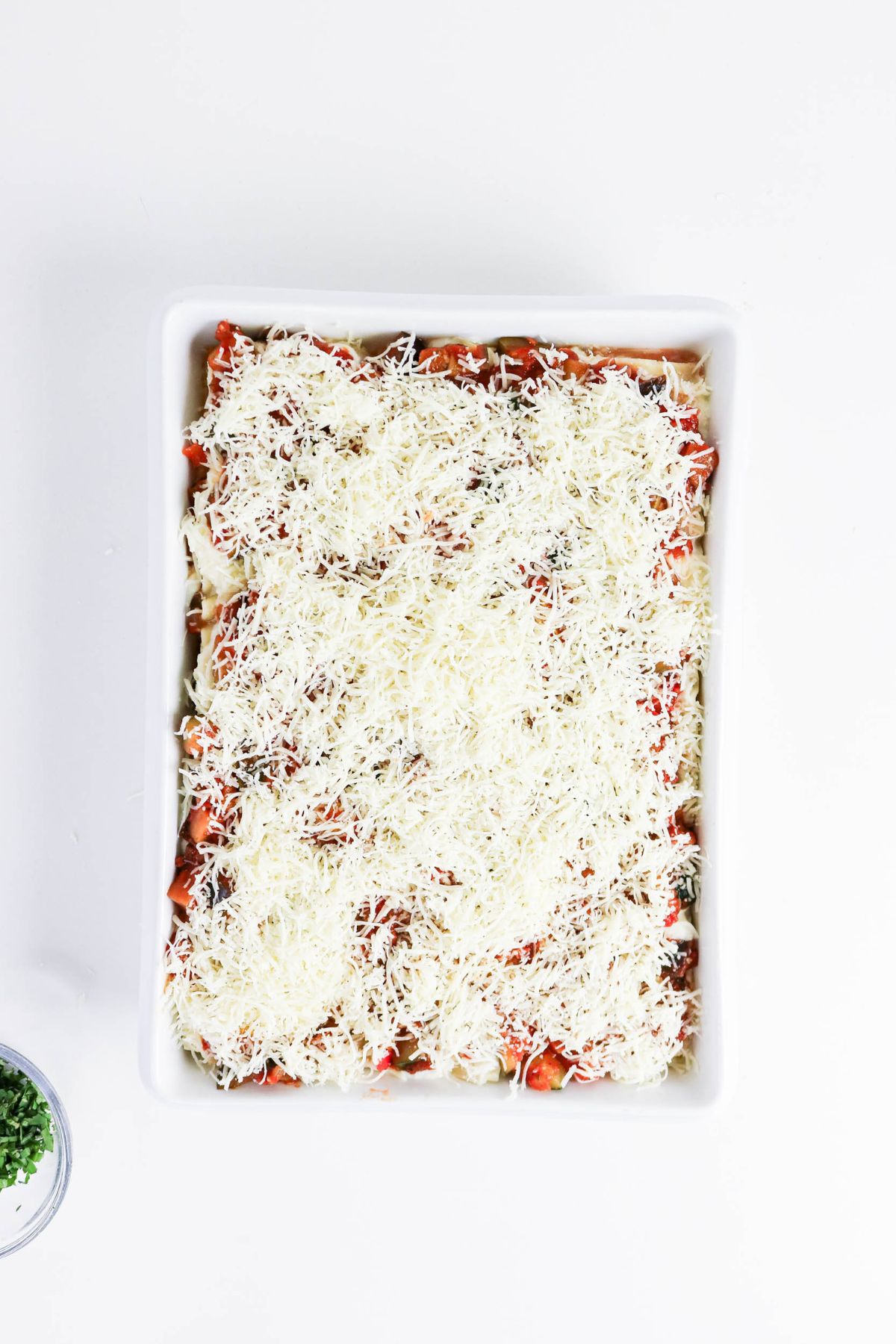 Rectangular baking dish filled with lasagna, topped with a layer of shredded cheese, photographed from above on a white background.