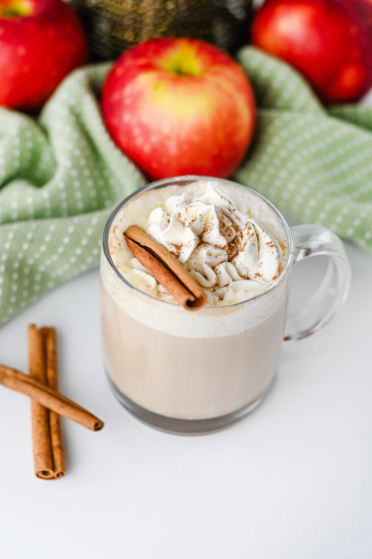 Apple chai latte in a glass mug topped with whipped cream and a cinnamon stick