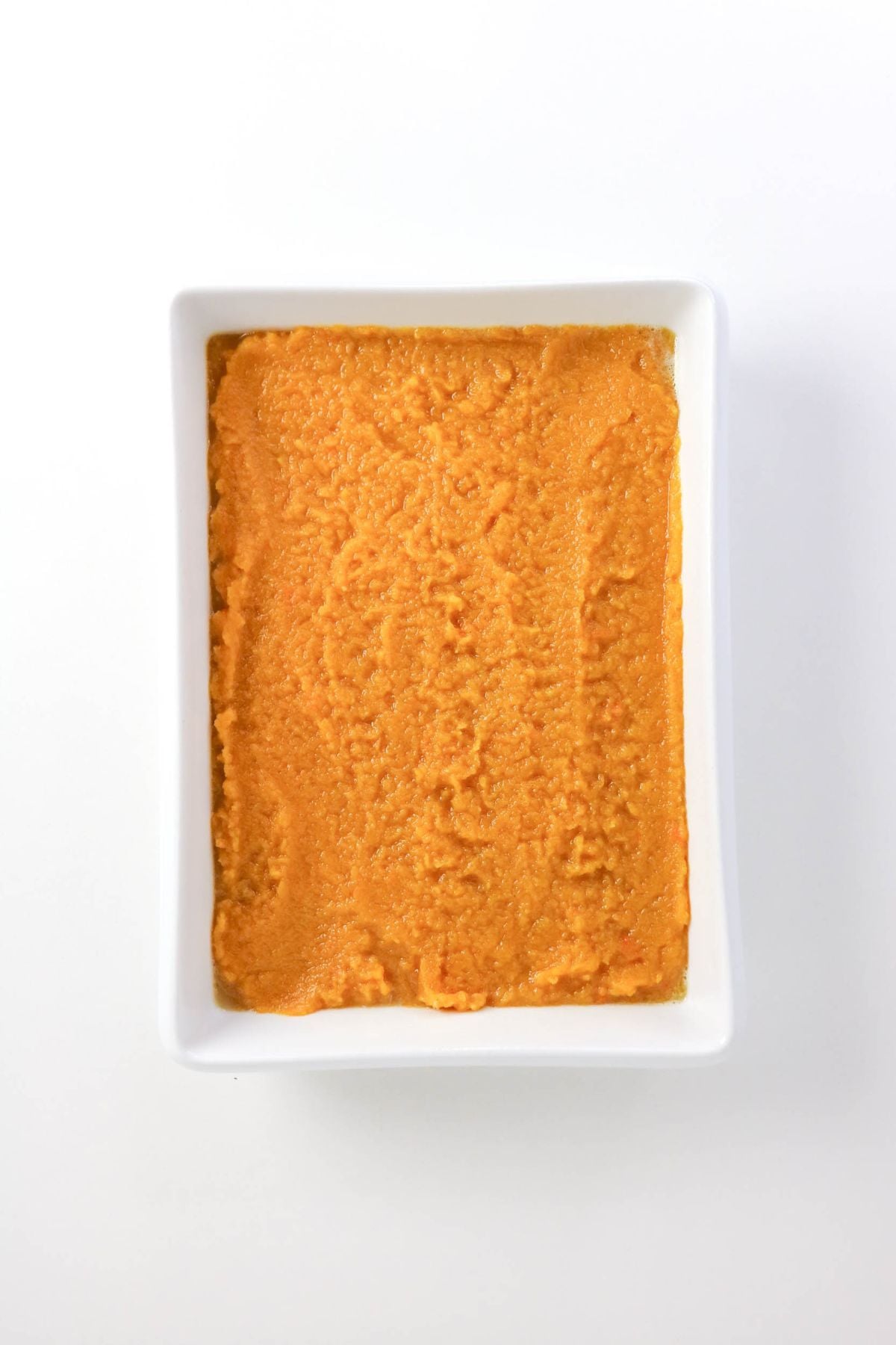 Rectangular white dish filled with a smooth, orange spread or dip, photographed from above on a plain white background.