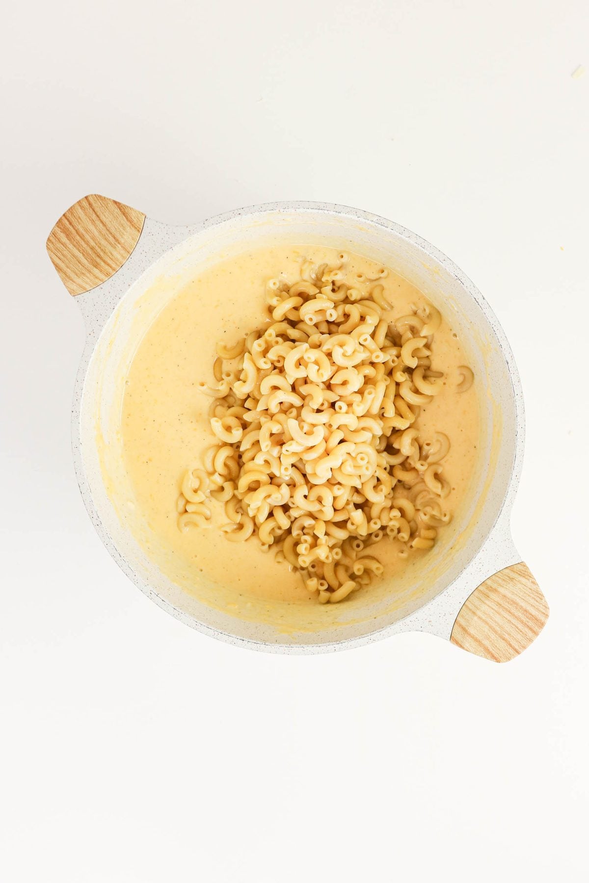 A white pot with cooked elbow macaroni resting on top of creamy cheese sauce, viewed from above on a white background.