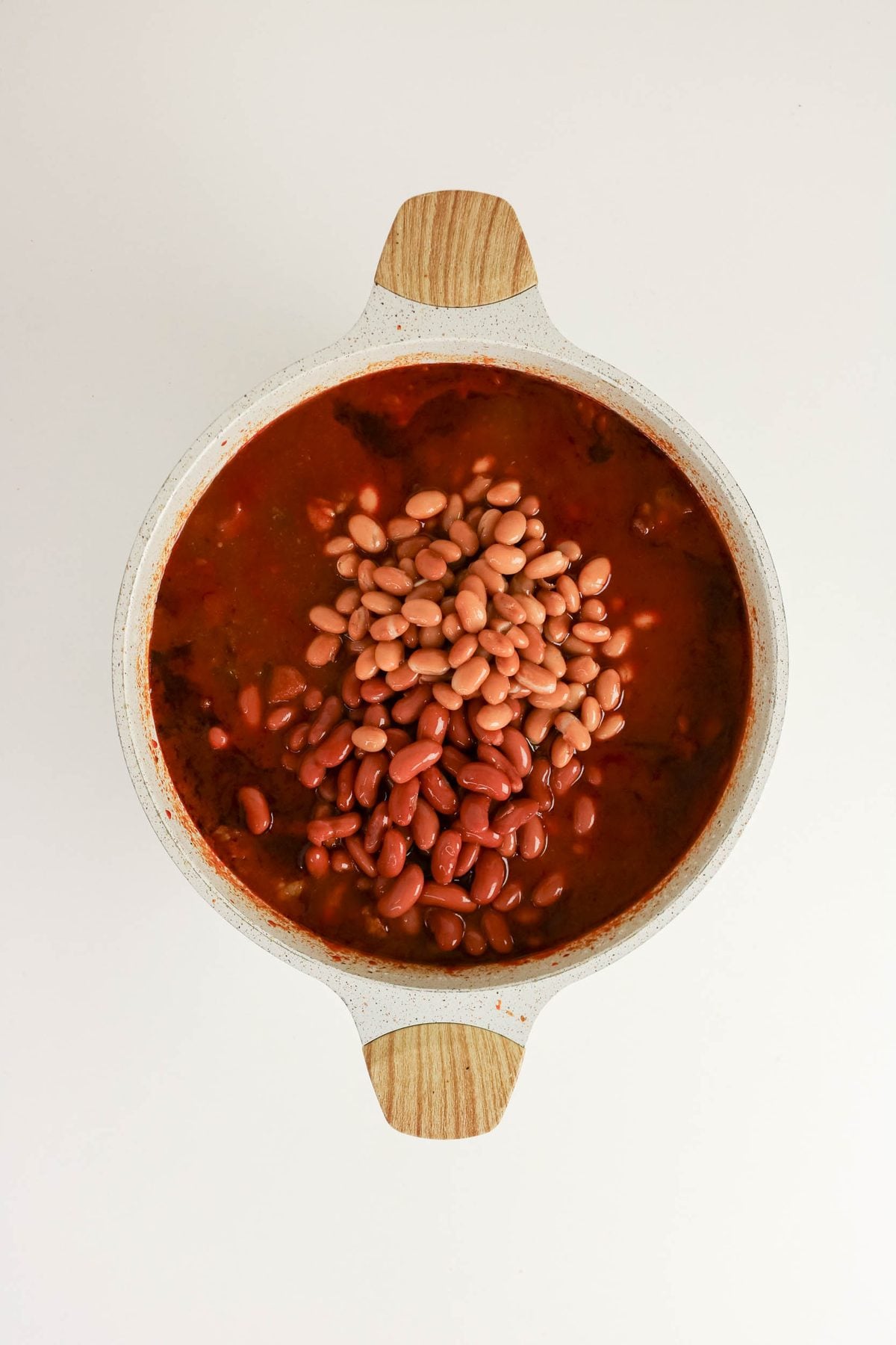 A white pot filled with chili topped with kidney and pinto beans, viewed from above on a plain white background.