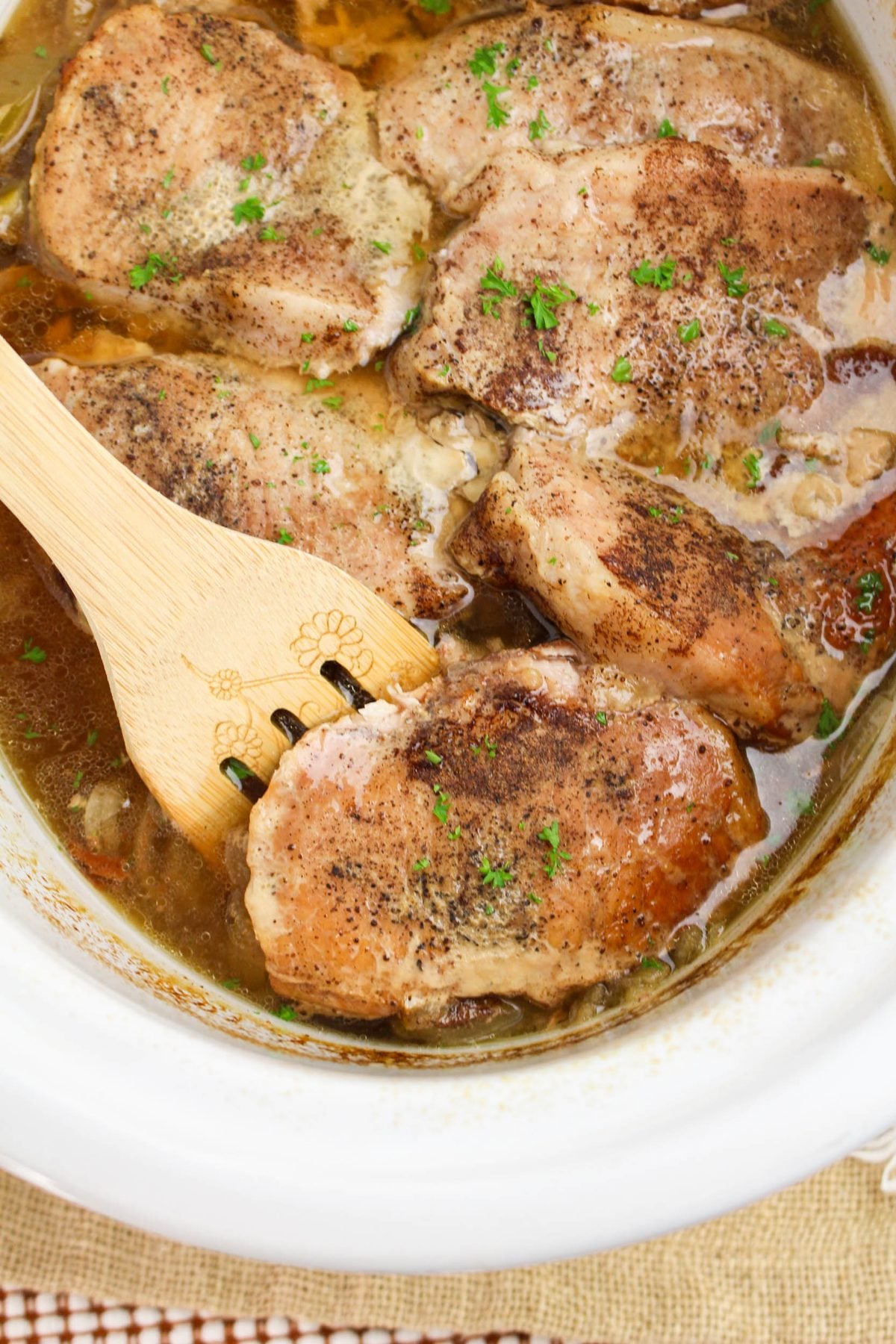 Crockpot apple pork chops in the slow cooker, seasoned and garnished with fresh parsley