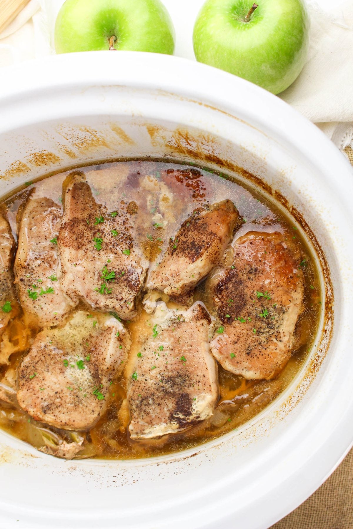 Crockpot apple pork chops simmering in the slow cooker with fresh green apples in the background