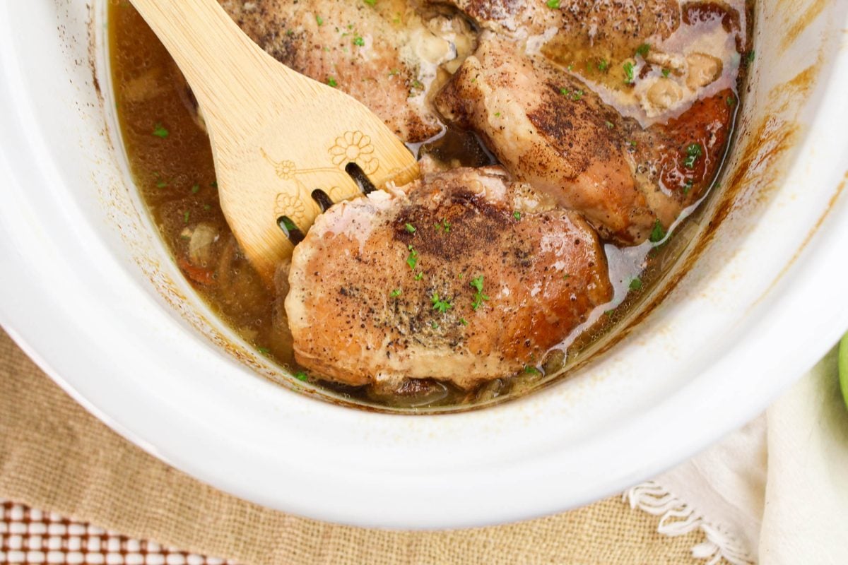 Lifting a tender crockpot apple pork chop with a wooden spoon from the slow cooker