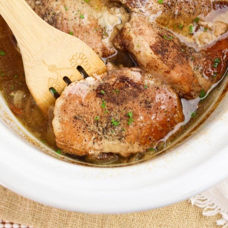 Crockpot apple pork chops in a slow cooker with a wooden spoon lifting one tender pork chop from the sauce