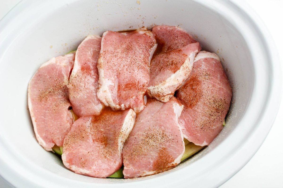 Step 4 for crockpot apple pork chops: pork chops coated with the apple cider spice sauce in the slow cooker, ready to cook