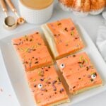 Four rectangular sugar cookie bars with orange frosting, sprinkles, and candy eyes are arranged on a white plate.