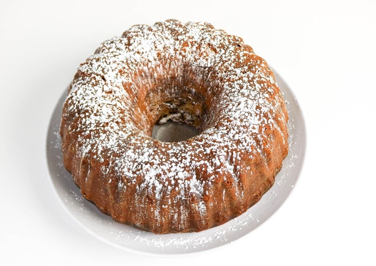 A Bundt cake dusted with powdered sugar sits on a white plate against a plain white background.