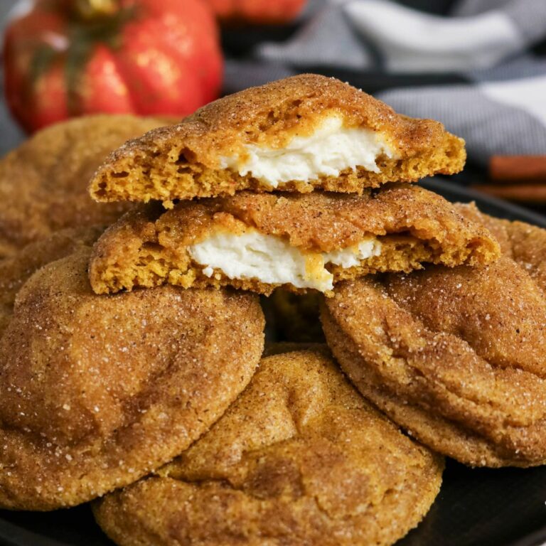A plate of round, cinnamon-dusted cookies with one cookie broken in half, revealing a creamy white filling inside.