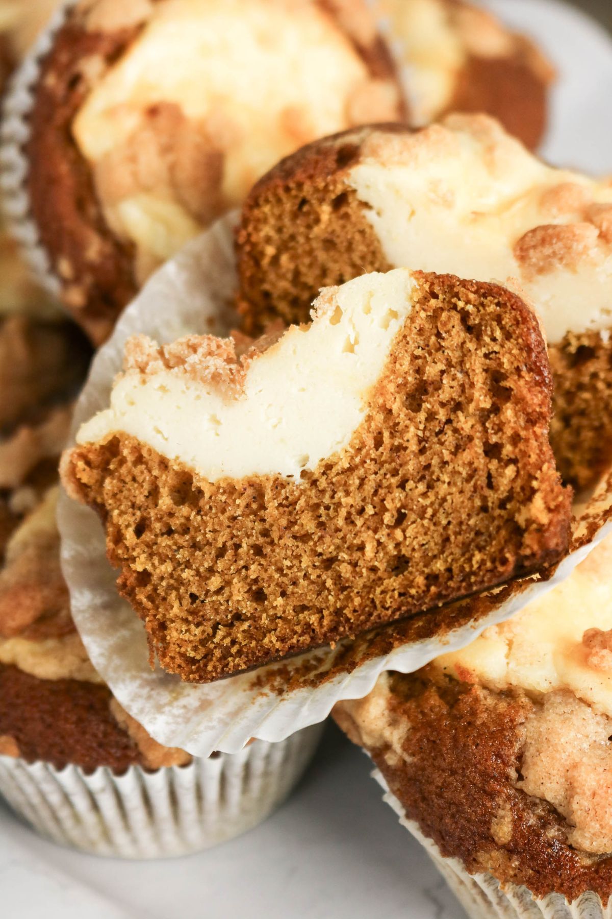 A sliced muffin with a creamy filling is displayed on a paper liner, showing its moist texture and swirled top.