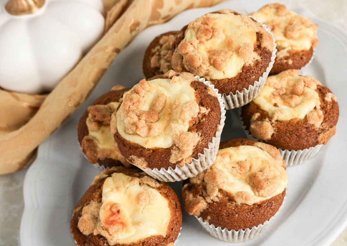 A plate of seven pumpkin muffins with cream cheese filling and crumb topping, arranged on a white dish.