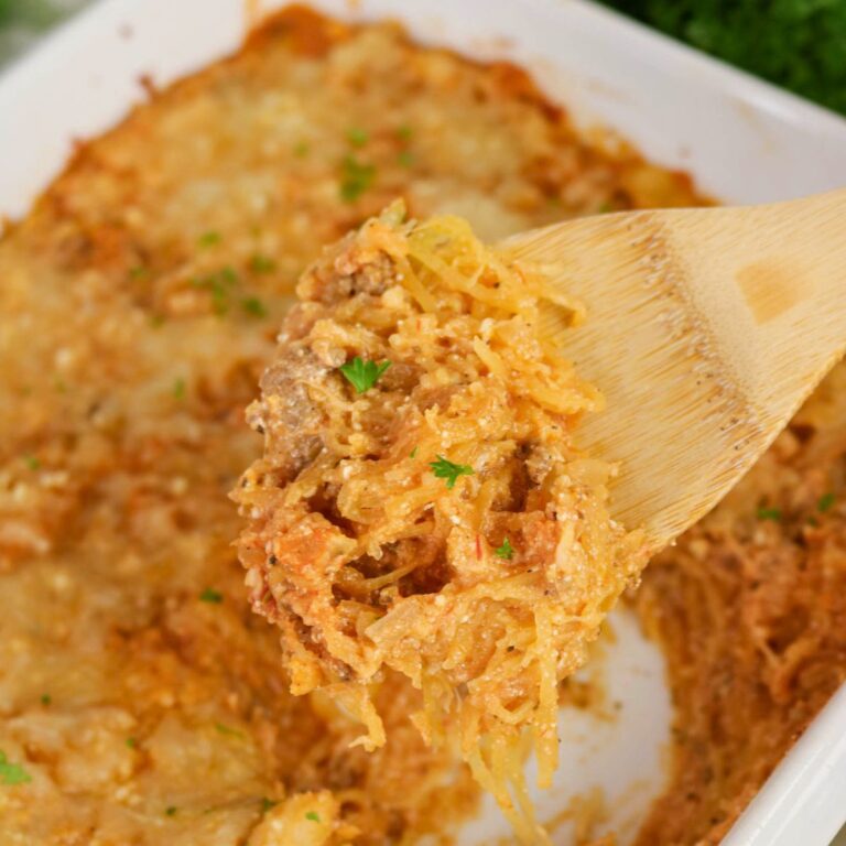 A wooden spoon holds a serving of cheesy baked spaghetti squash casserole above a white baking dish.