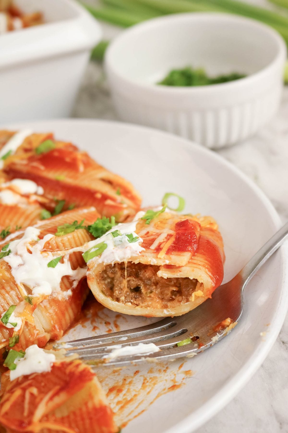 Stuffed pasta shells filled with meat and topped with tomato sauce and cream, served on a white plate with a fork.