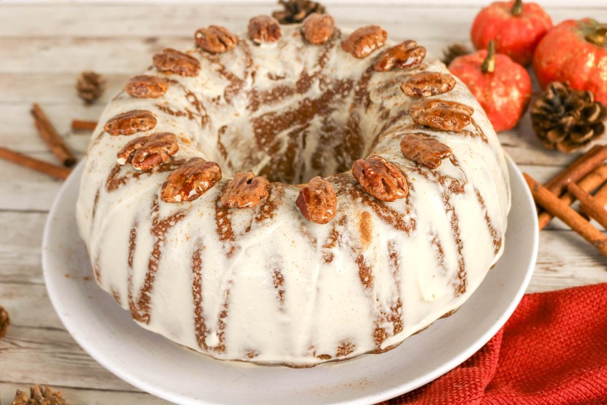 A bundt cake glazed with white frosting and topped with candied pecans.