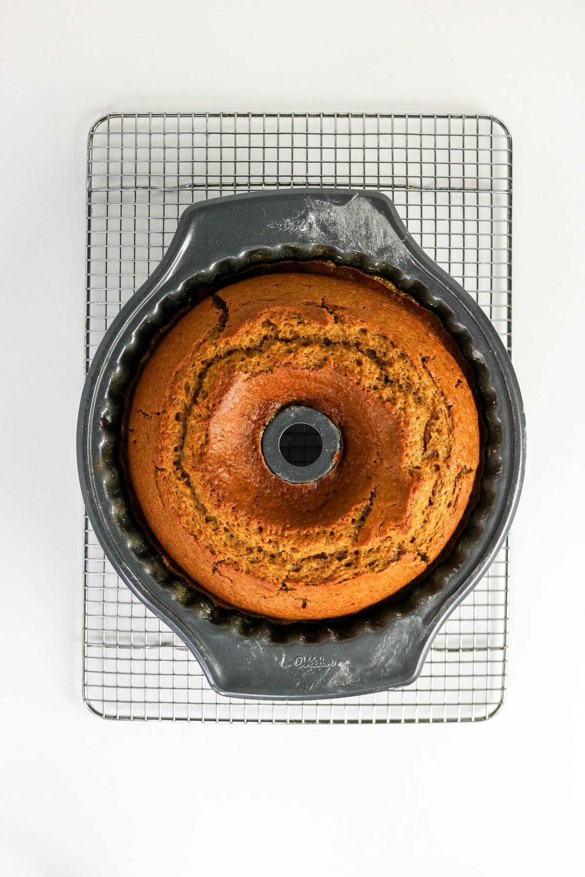A golden-brown bundt cake in a fluted pan, sitting on a wire cooling rack.