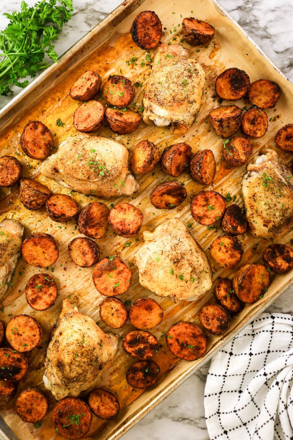 Sheet pan with roasted chicken thighs and halved baby potatoes, garnished with herbs.