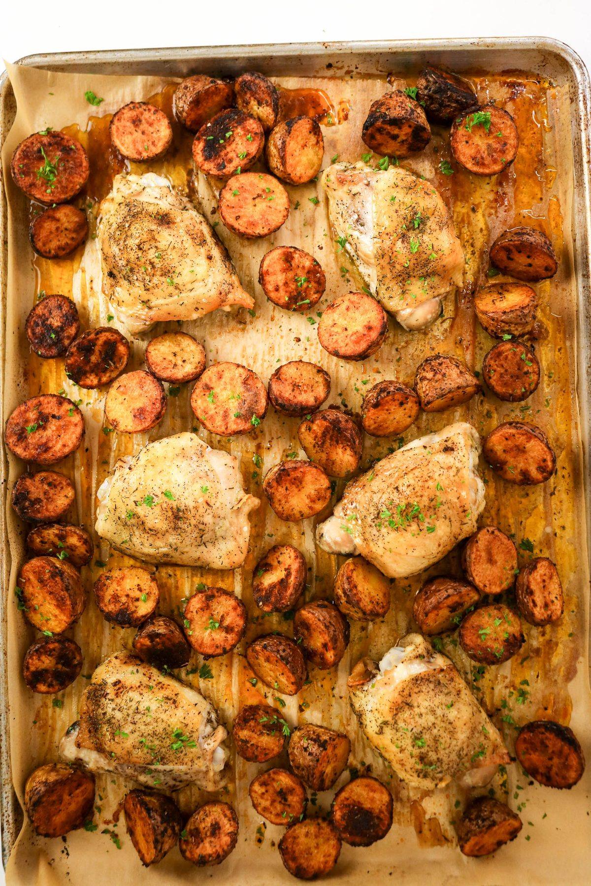 Sheet pan with roasted chicken thighs and halved baby potatoes, sprinkled with herbs.