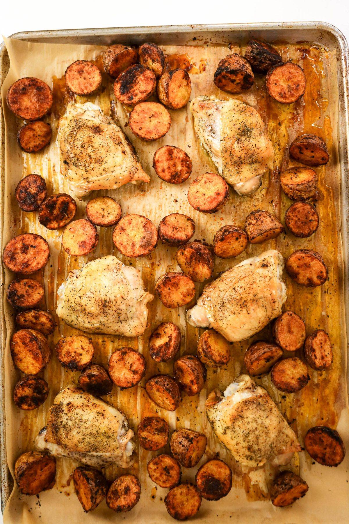 Sheet pan of roasted chicken thighs and halved red potatoes.