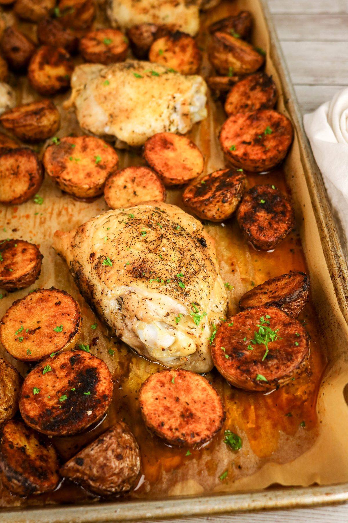 Roasted chicken thighs with halved red potatoes on a baking sheet.