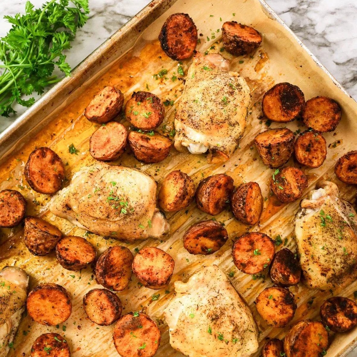 Roasted sheet pan chicken thighs and halved potatoes on a parchment-lined baking sheet.