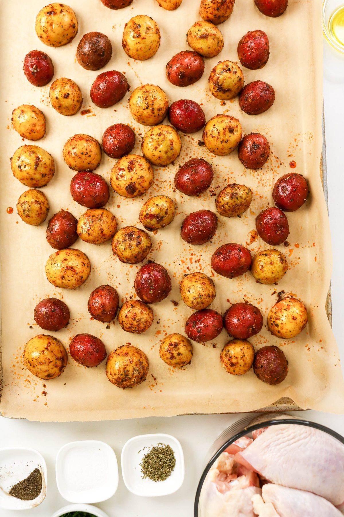 Seasoned red and gold baby potatoes spread out on a parchment-lined baking sheet.